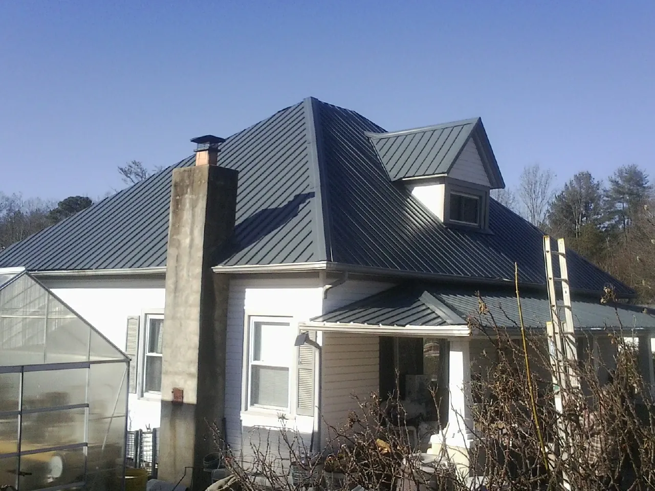 Dark blue standing seam metal roof on a white farmhouse with dormer — Slate & Tile Roof Repair by Roofing Brothers in Alvarado