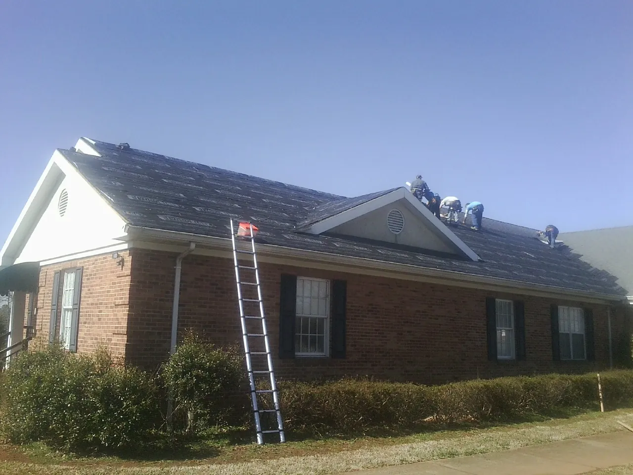 Crew tearing shingles off a brick ranch roof with a ladder set — Emergency Roof Repair work by our crew in Alvarado