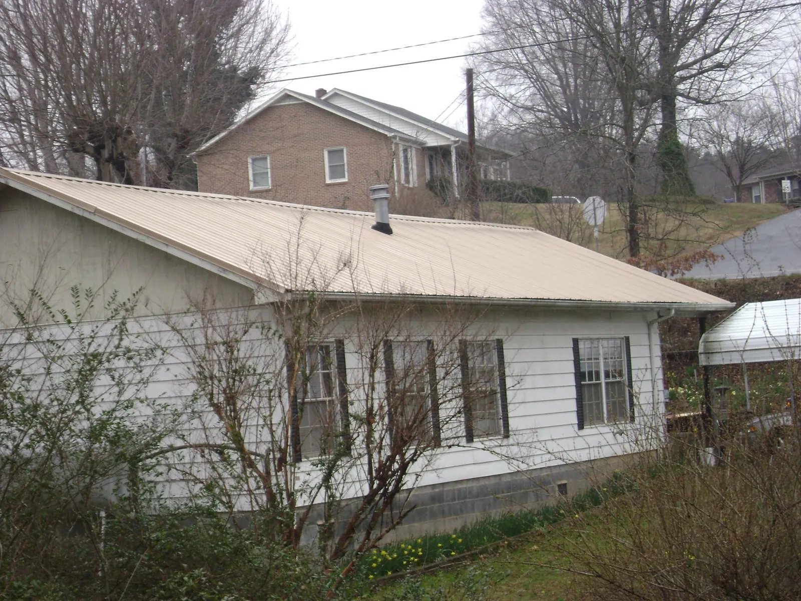 Tan metal roof on a white sided house set into a hillside in Alvarado