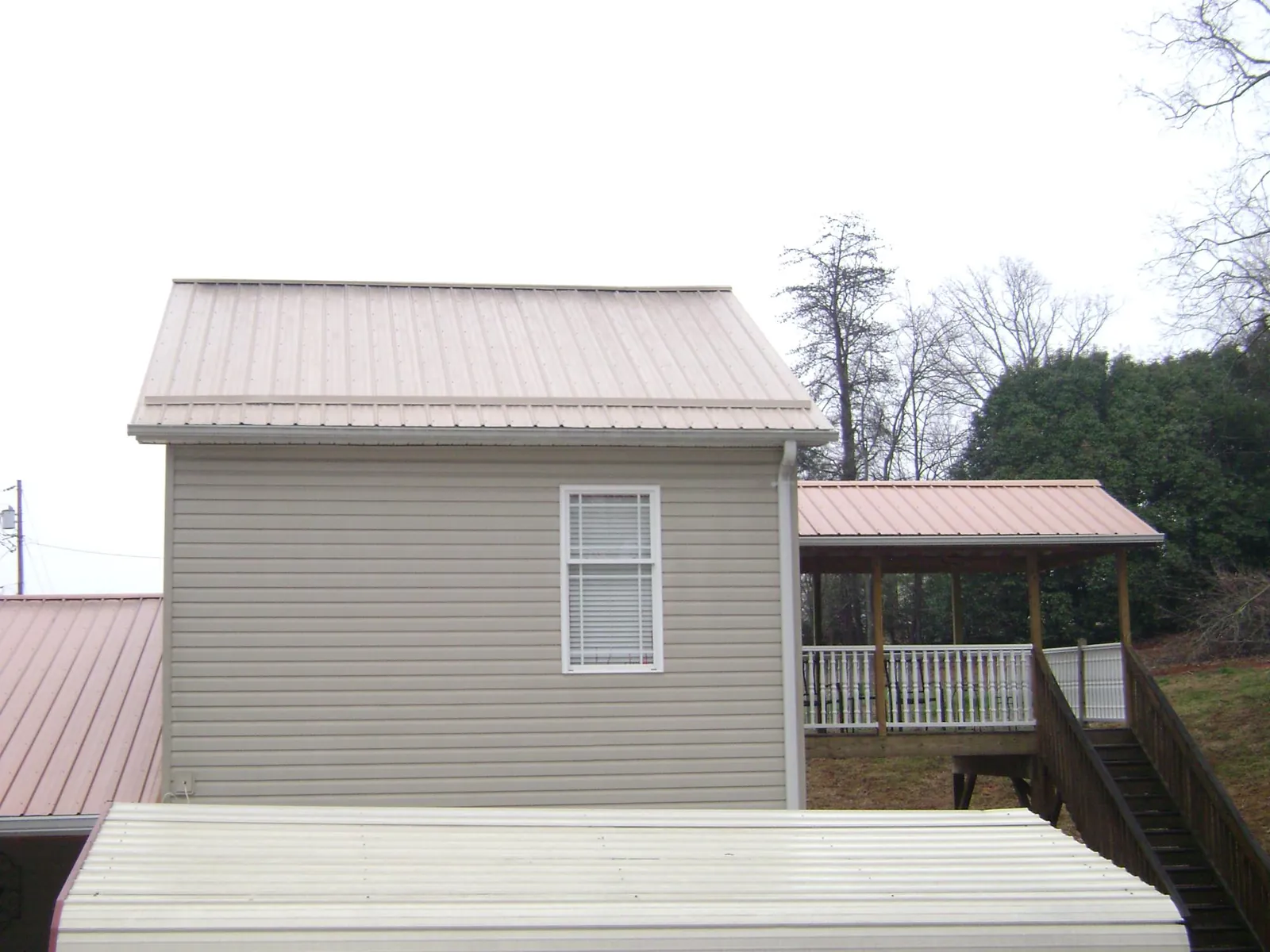 Tan metal roofs on a two story addition and attached porch, from a Roof Replacement job in Alvarado